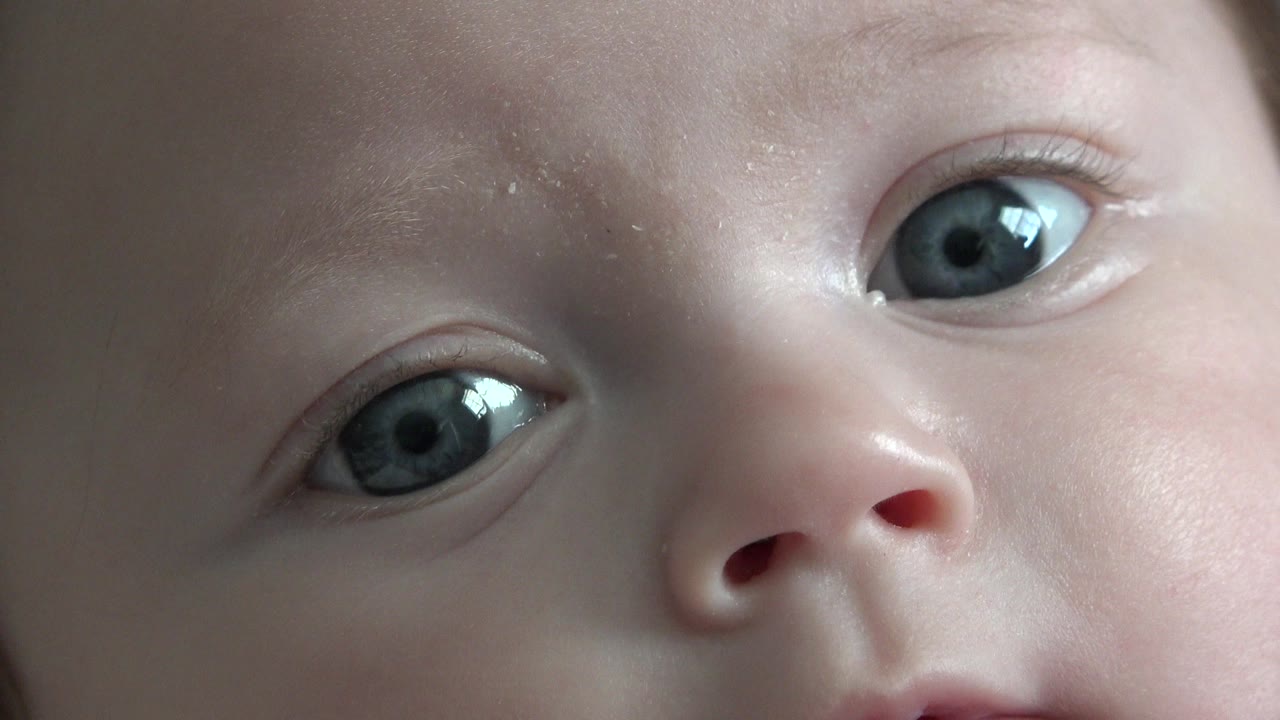 At 0:00, a baby in Westminster, Colorado fills the frame with both blue eyes visible, a small nose near center, and soft neutral background around the face.