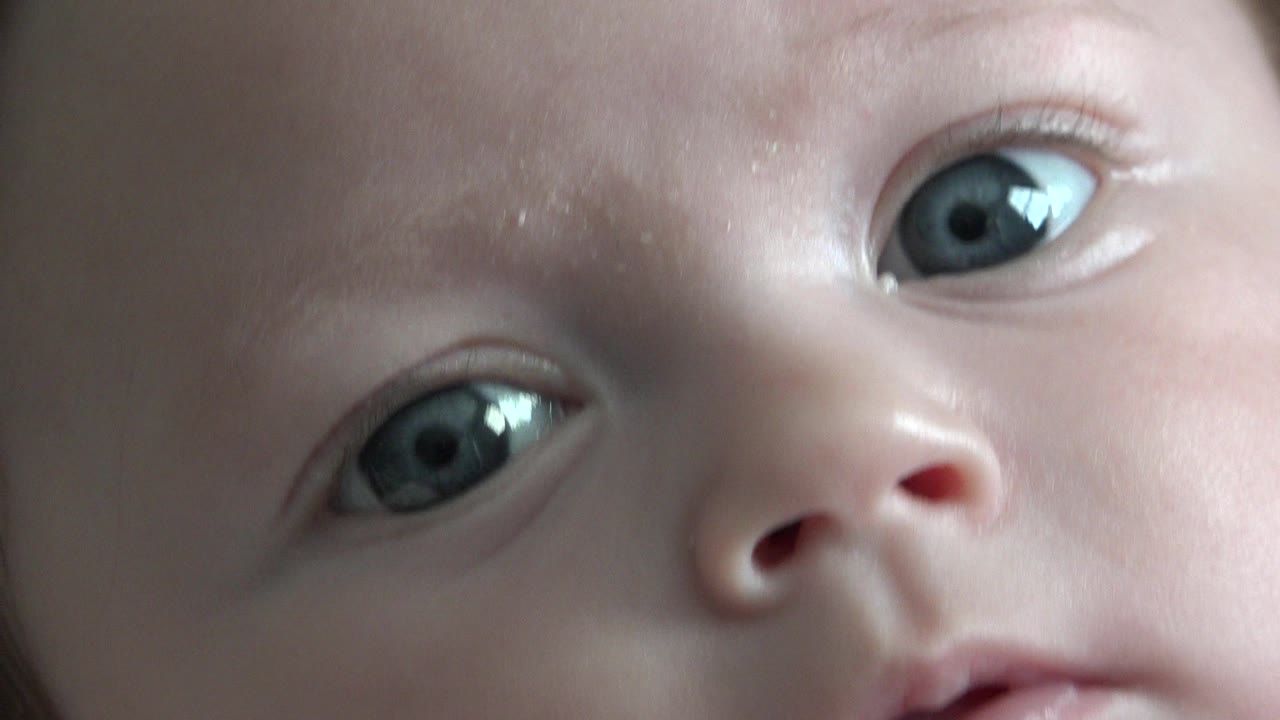 At 0:01, the infant's gaze stays near the lens, with the face angled diagonally and the nostrils and eyes sharply framed in the close view.