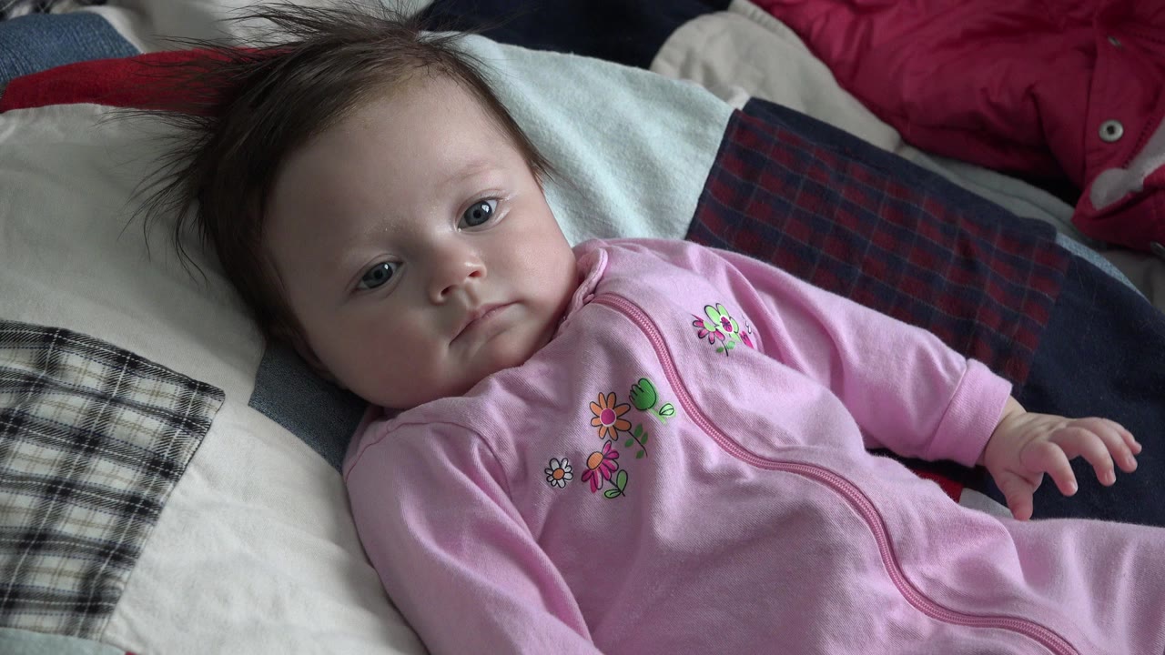 Baby in a pink sleeper lying on a patchwork quilt.