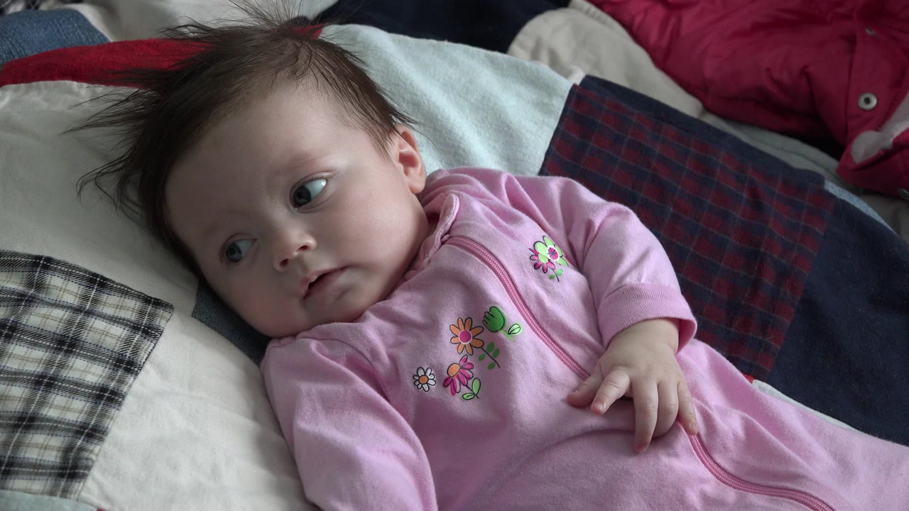 Baby in a pink sleeper lying on patterned bedding.