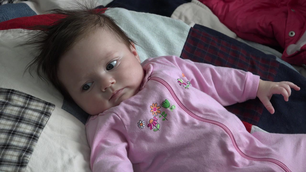 Baby in a pink sleeper lying on a patchwork quilt.