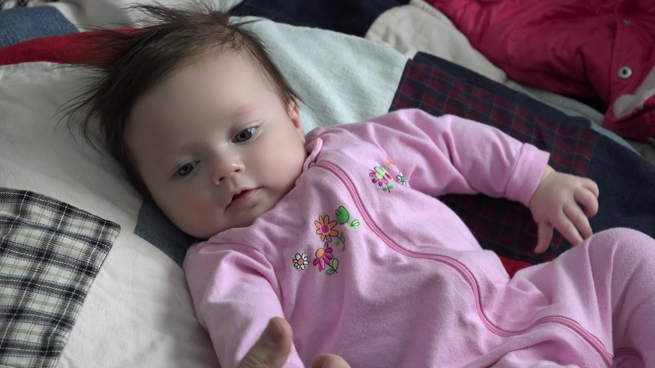 Baby in pink clothing glancing downward on a bed.