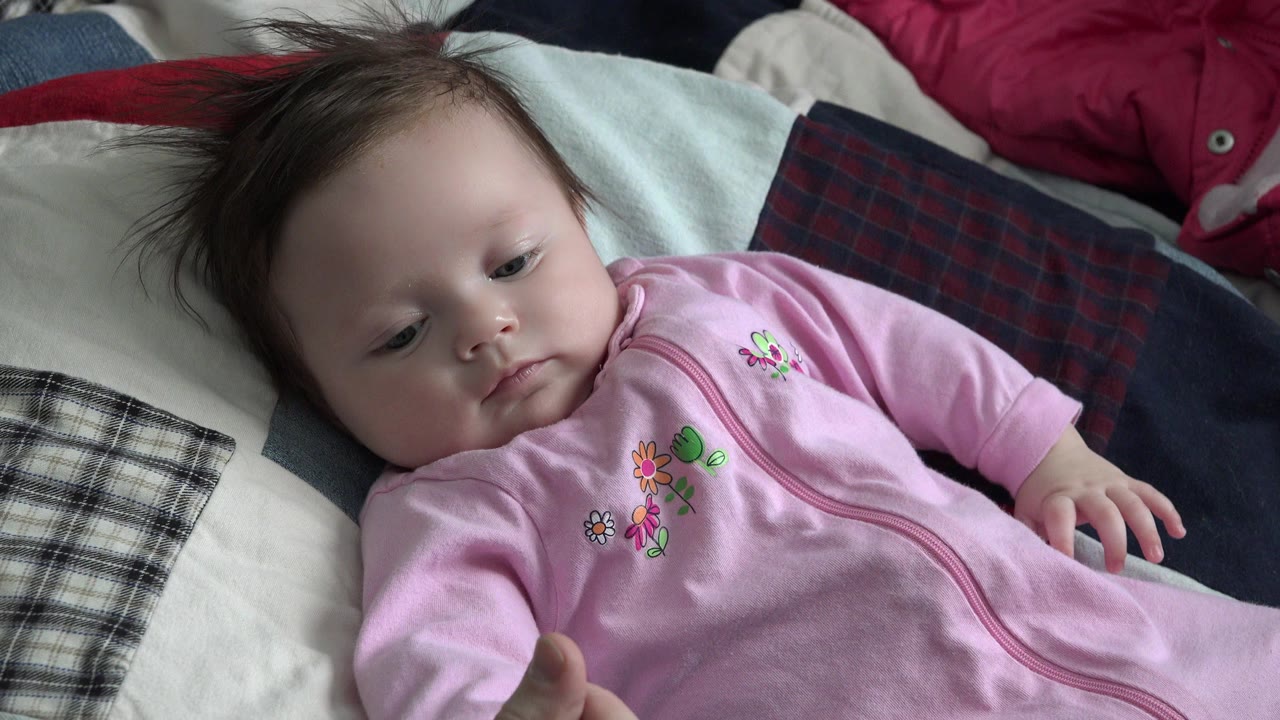 Baby in a pink onesie lying on patterned bedding