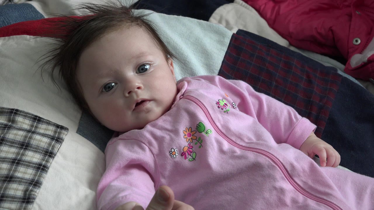 Baby in a pink sleeper lying on patterned pillows.