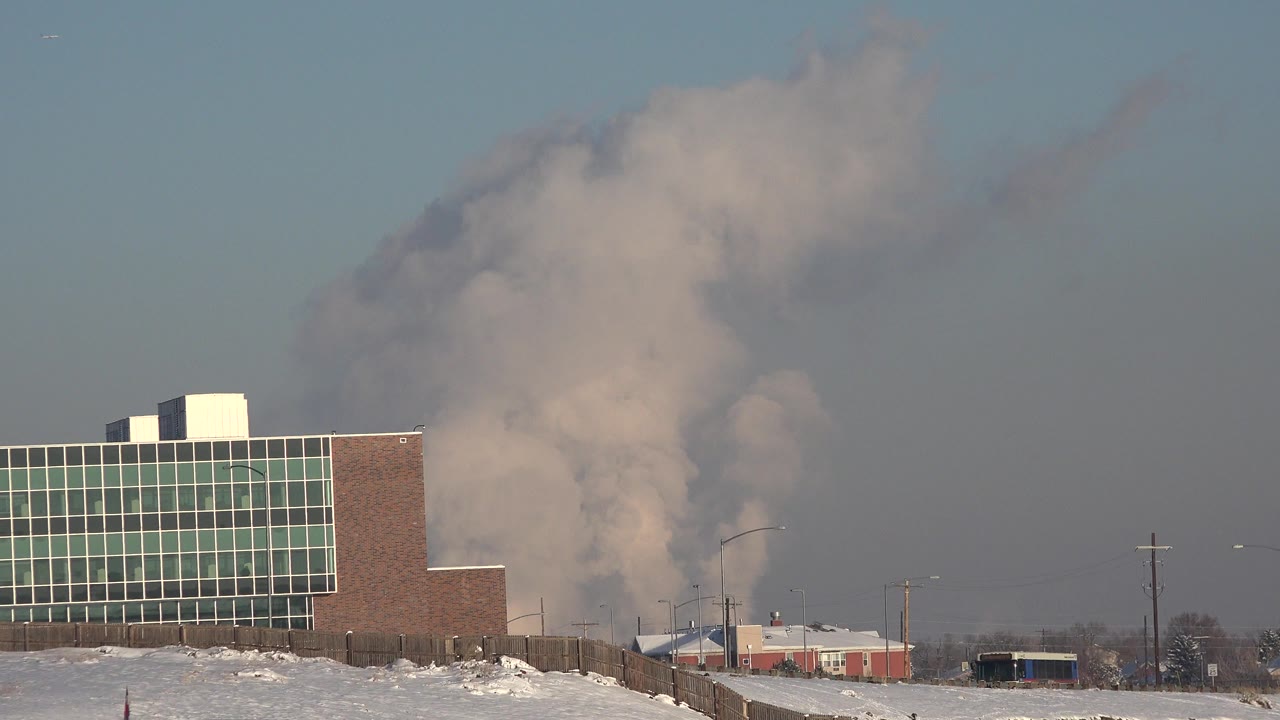In Westminster, Colorado, a brick and glass industrial building stands beside snowy ground as a beige gray smoke plume rises behind it, with no visible people.