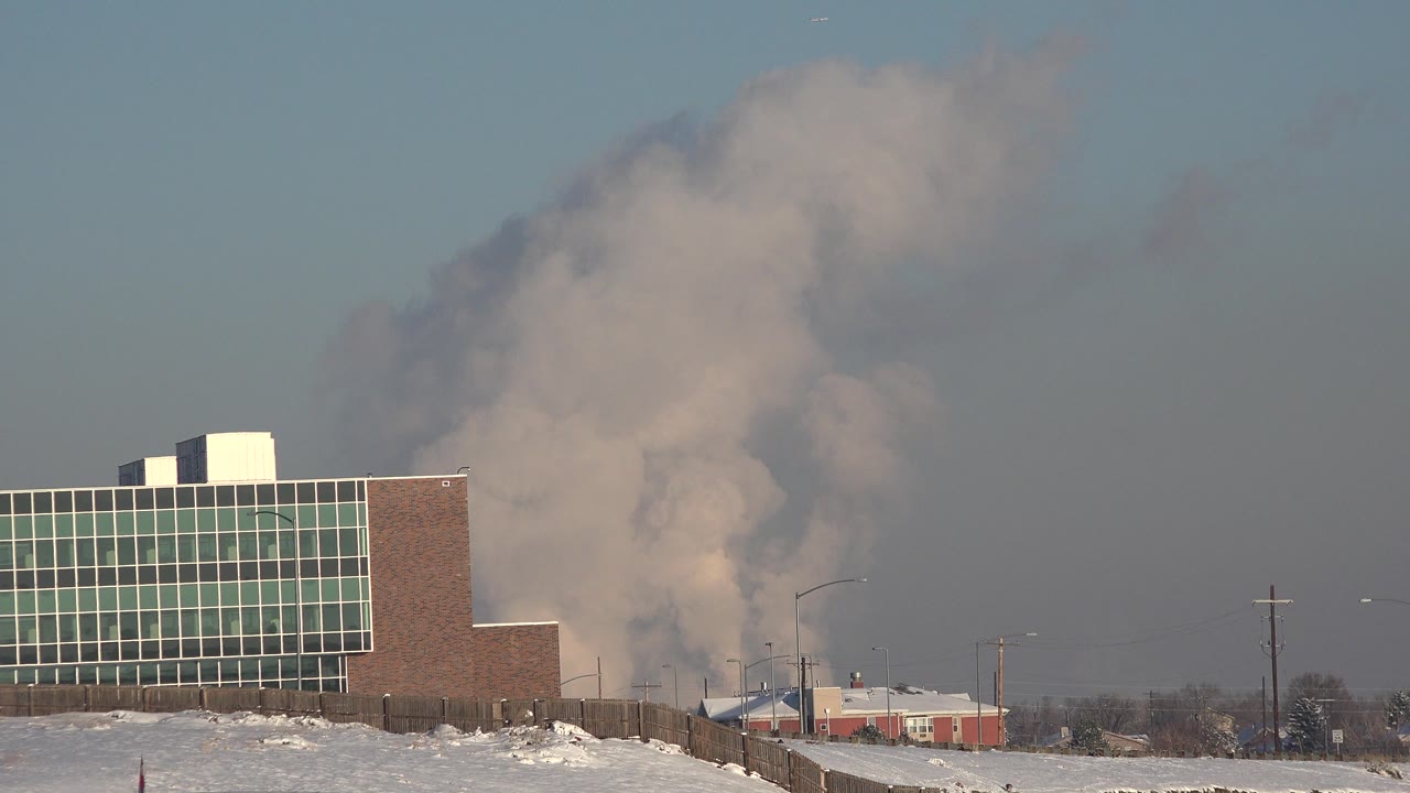At 0:00 in Westminster, Colorado, a green-windowed industrial building sits at left while a large smoke plume rises behind low structures, with snow on the ground and no visible people.