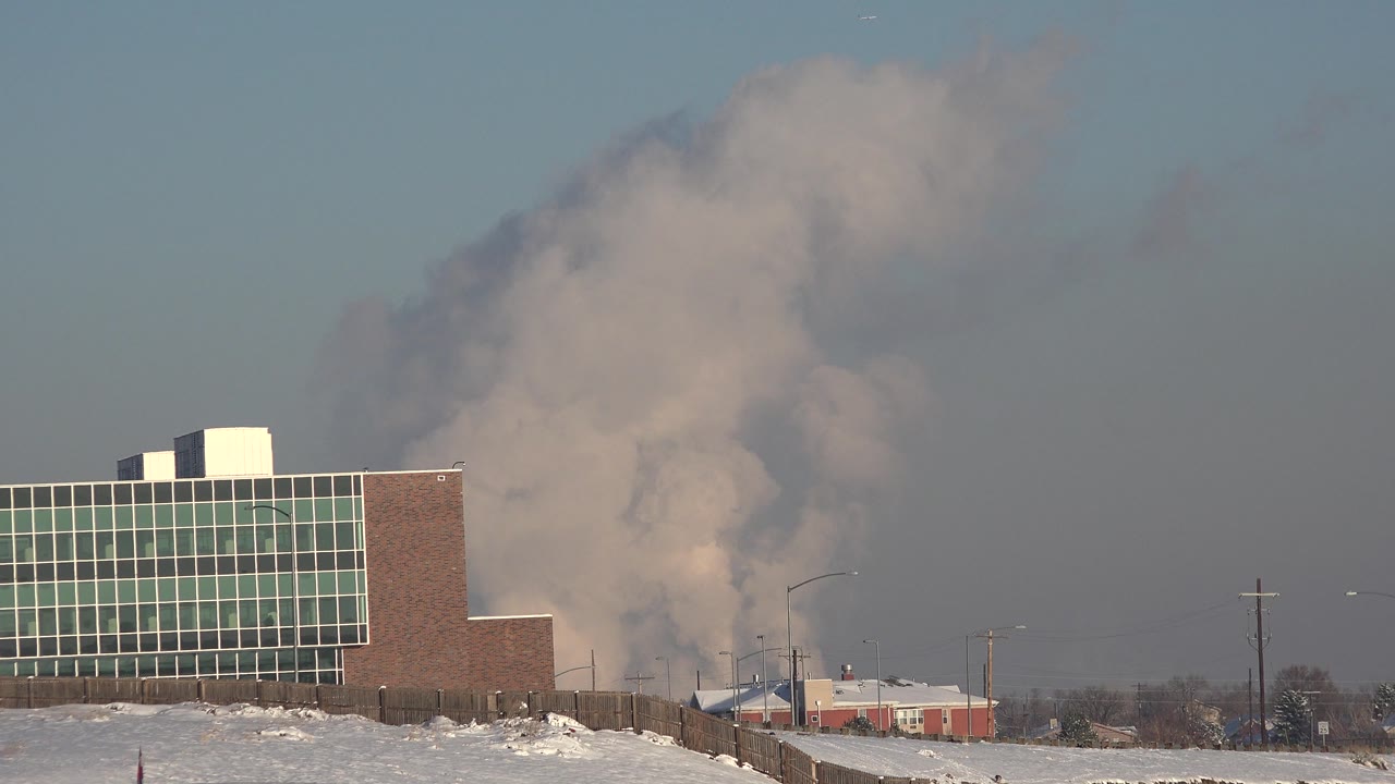 Industrial building in front of thick smoke under blue sky.