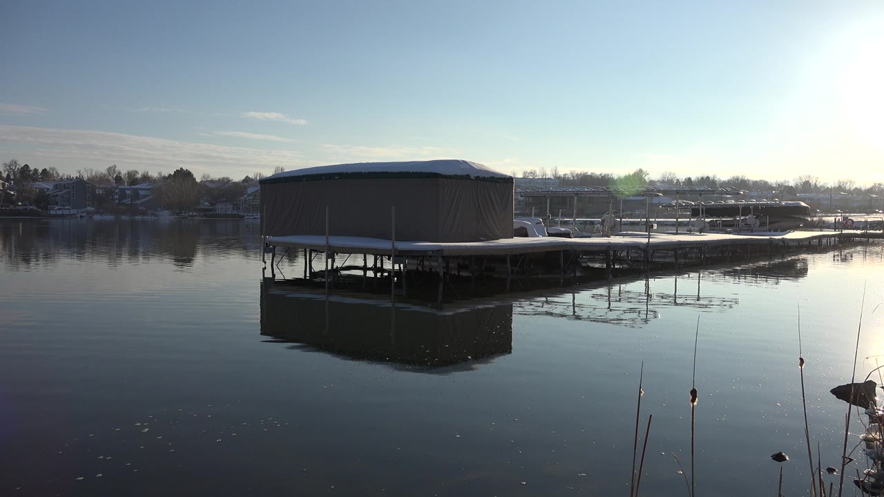 The Westminster lake view holds on the covered dock, with strong sun glare at upper right and smooth water reflecting the structure.