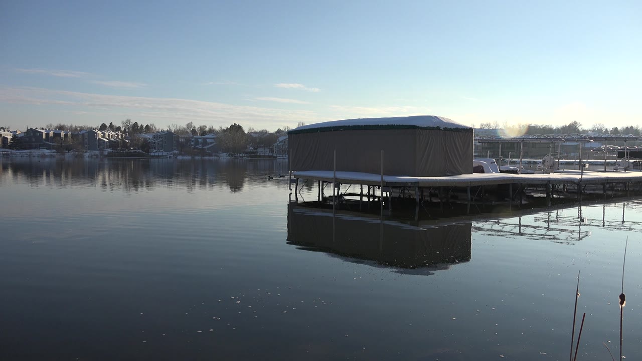 Dock building on the right side of a calm lake with reflections across the water.