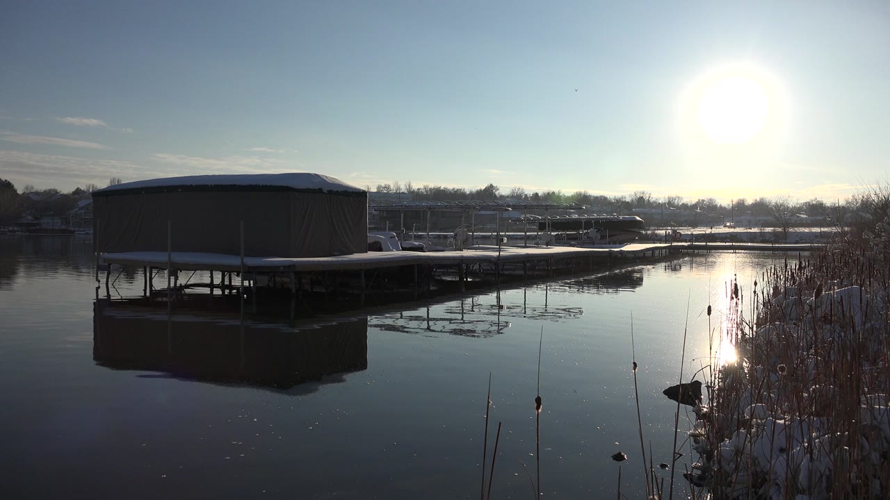 Covered boat dock on a calm winter lake under bright sun.