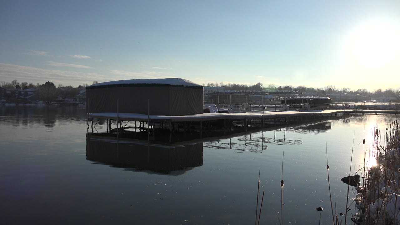 Covered dock over still winter lake water with bright sun glare.