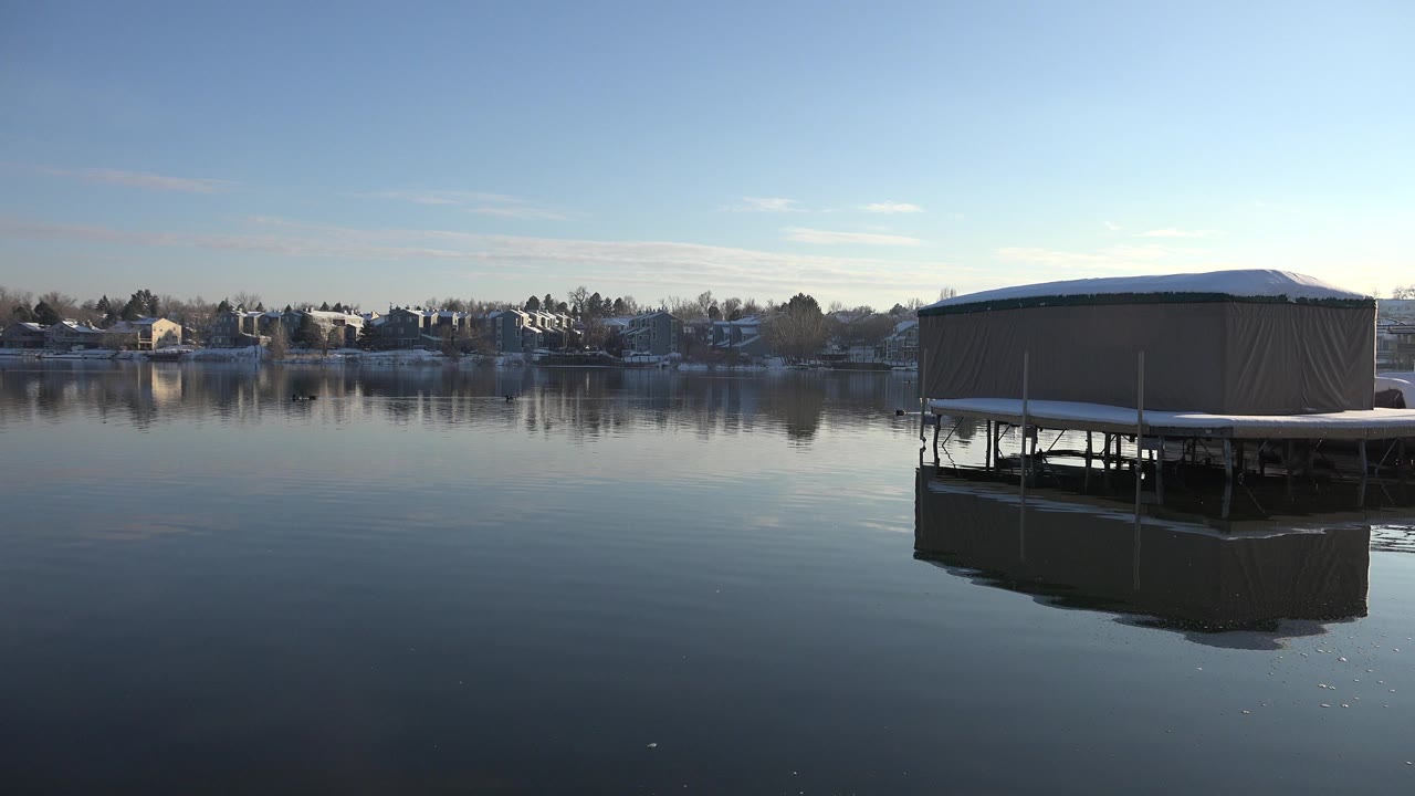 Tan covered platform over calm water with distant snowy homes.