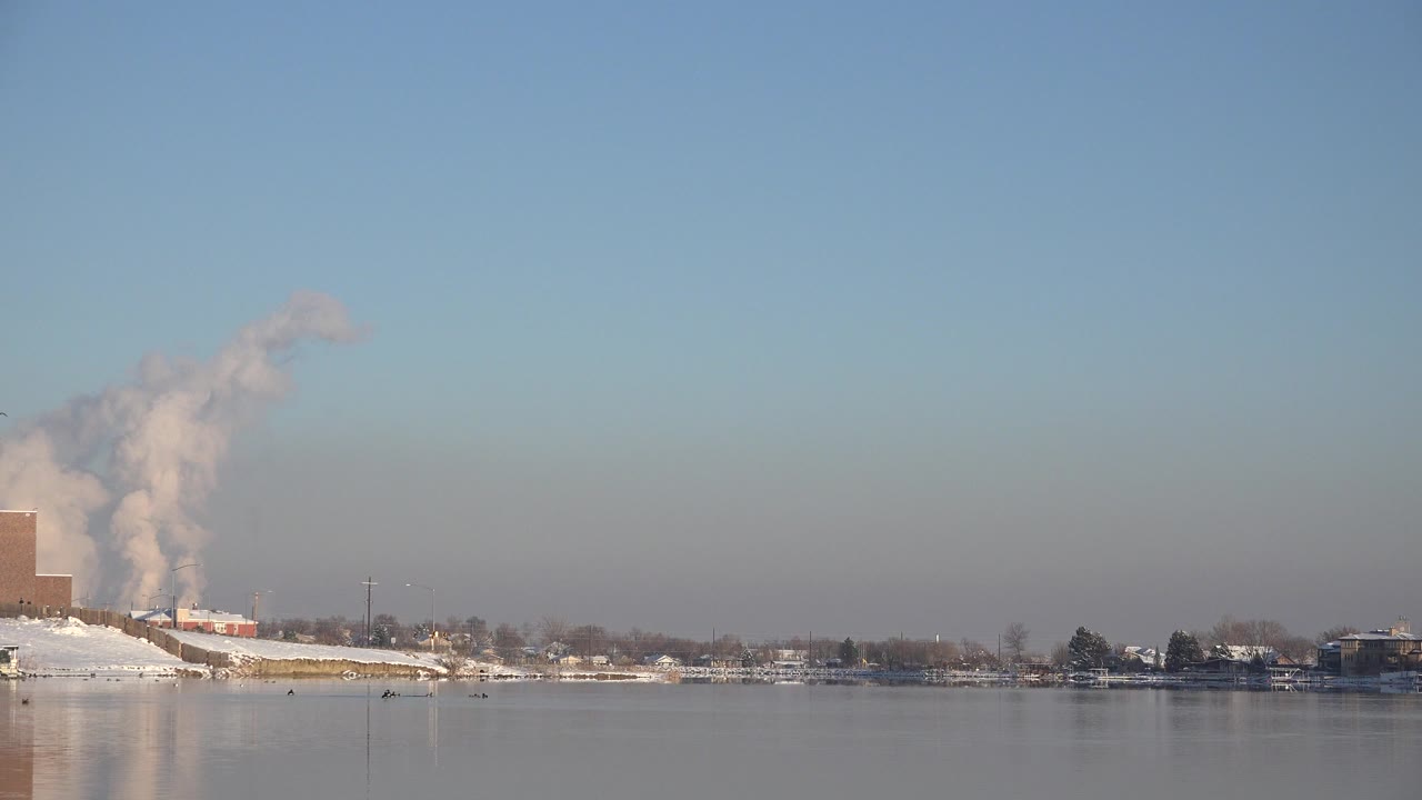 Wide snowy waterfront with distant plume and buildings