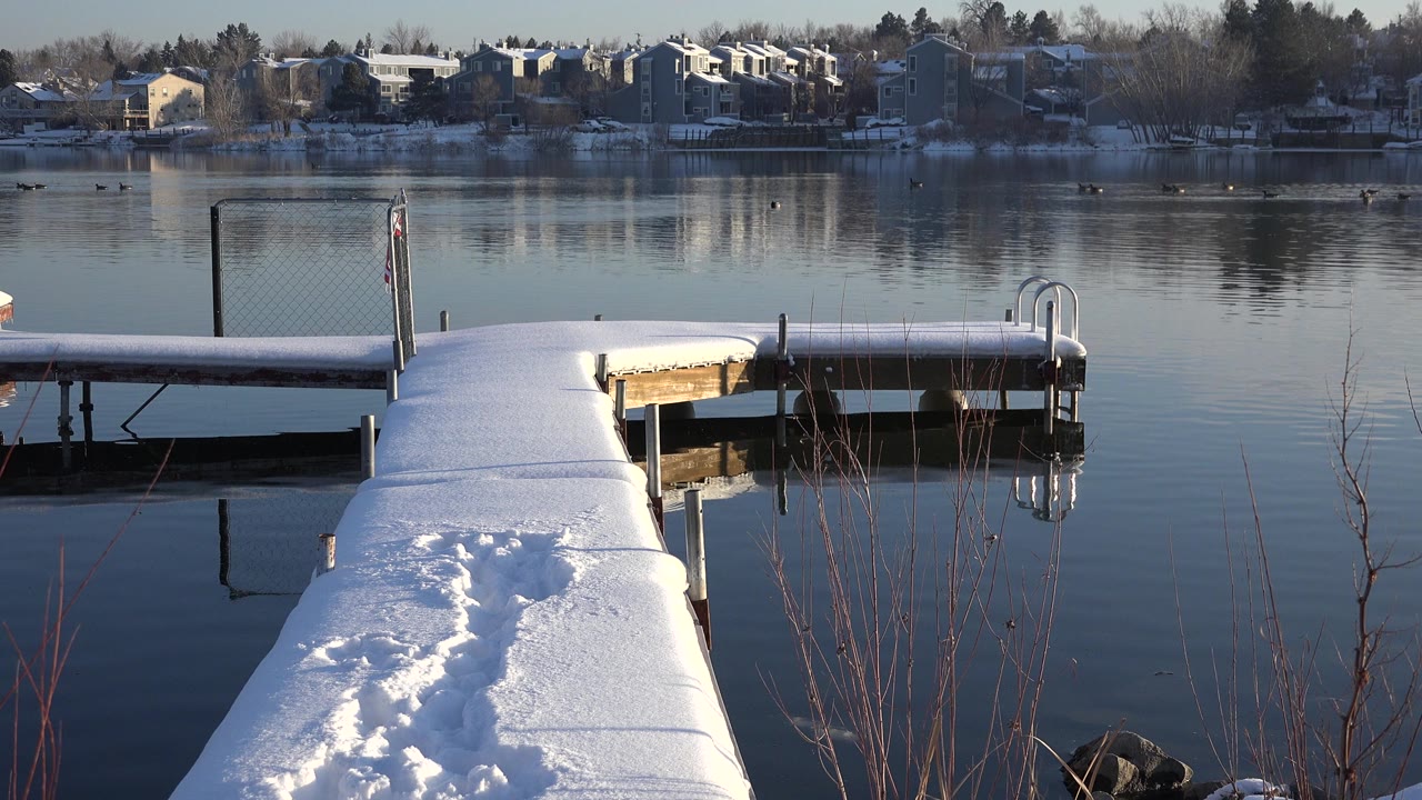 Snow-covered pier with footprints beside calm lake water