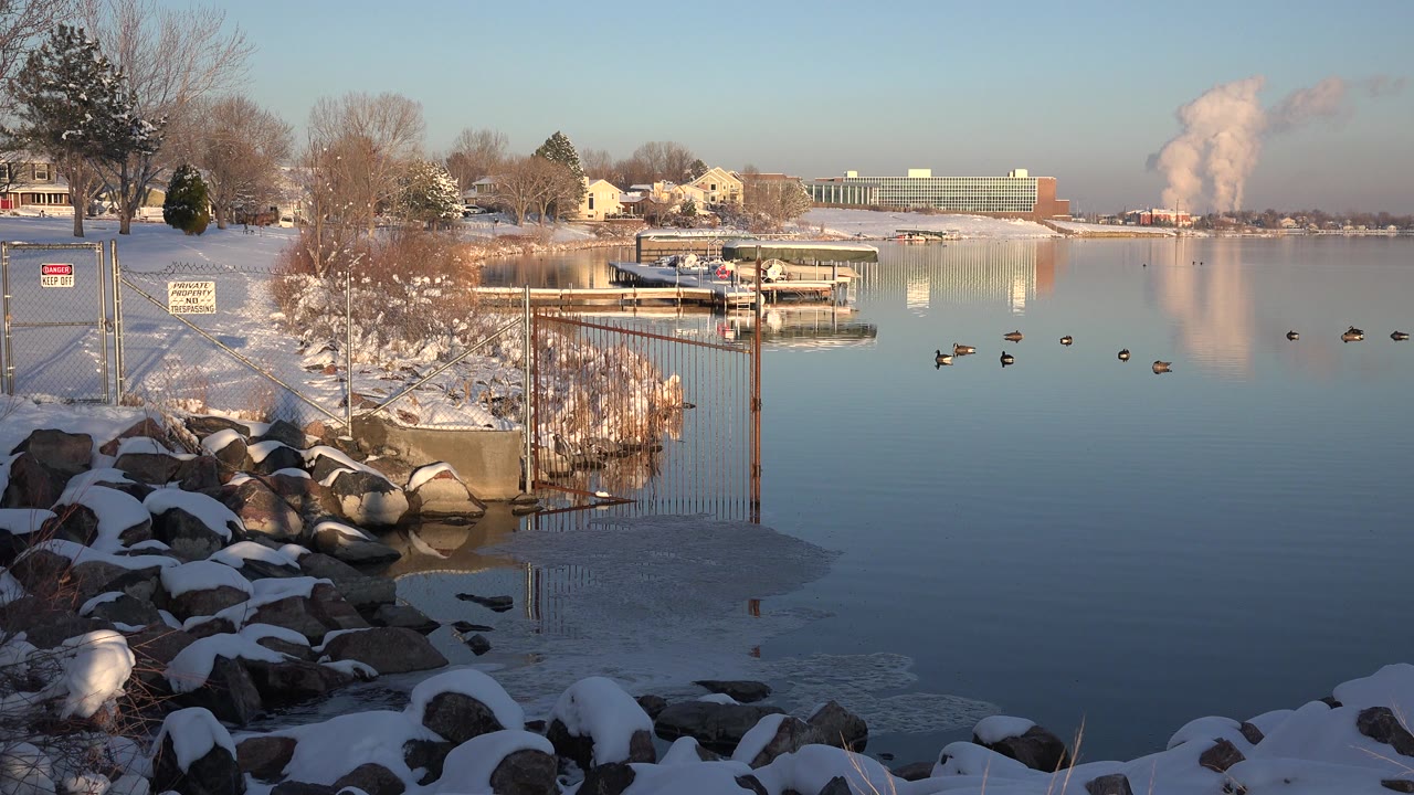 Snowy rocks beside a blue lake with docks and waterfowl
