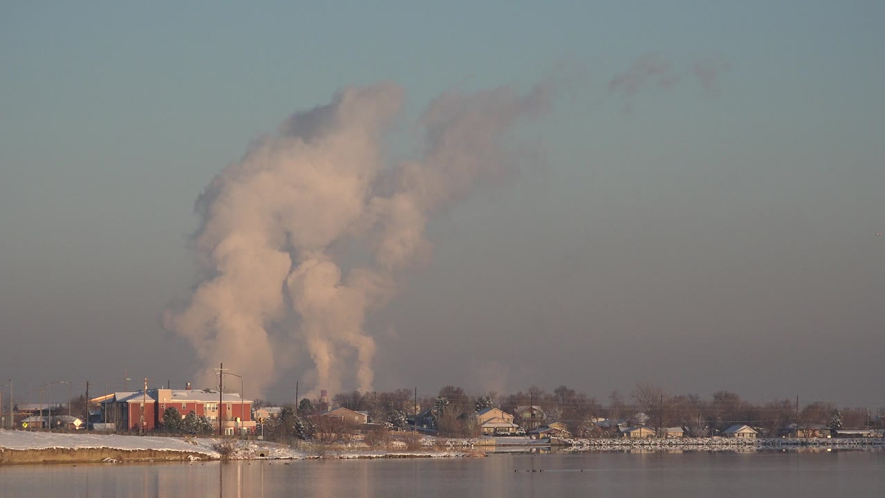 Industrial smoke plume over a shoreline across calm water.