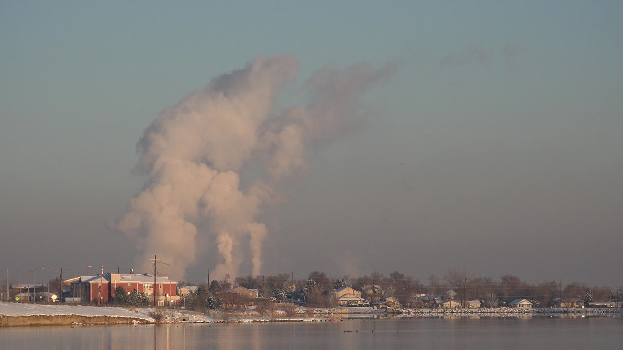 At 0:01, the smoke column appears broad and dense over the Westminster shoreline, with the red building left of center, low houses, bare trees, and no visible people.
