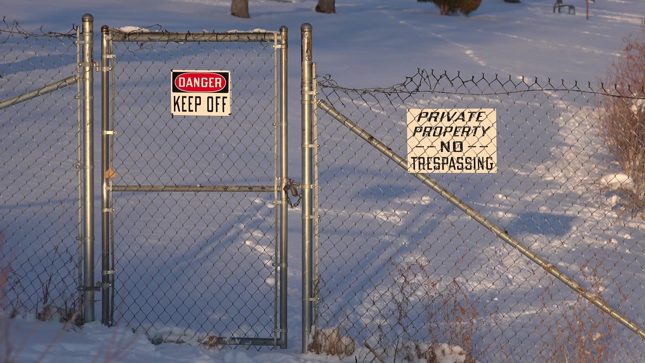 Chain-link fence with Danger Keep Off and Private Property No Trespassing signs in snow.
