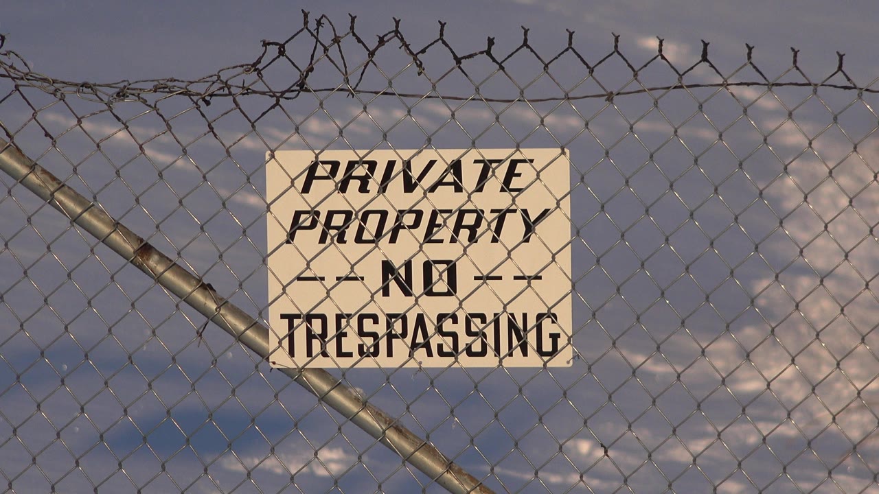 At 0:00, a beige Private Property No Trespassing sign is centered on a chain-link fence in Westminster, Colorado, with barbed wire above and no visible people.