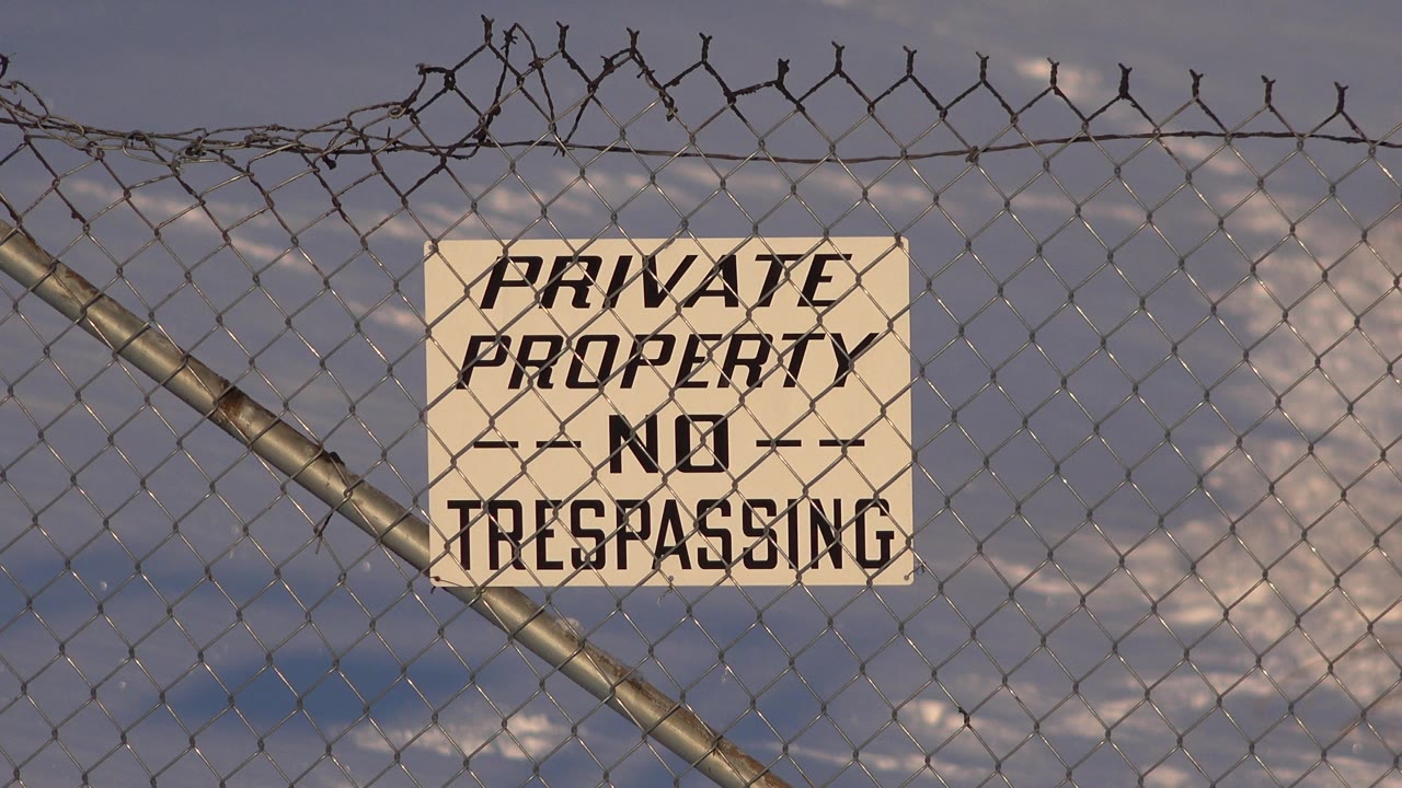 At 0:01, the no trespassing sign remains near center on the fence, with the diagonal post crossing from lower left toward the sign and no visible people.
