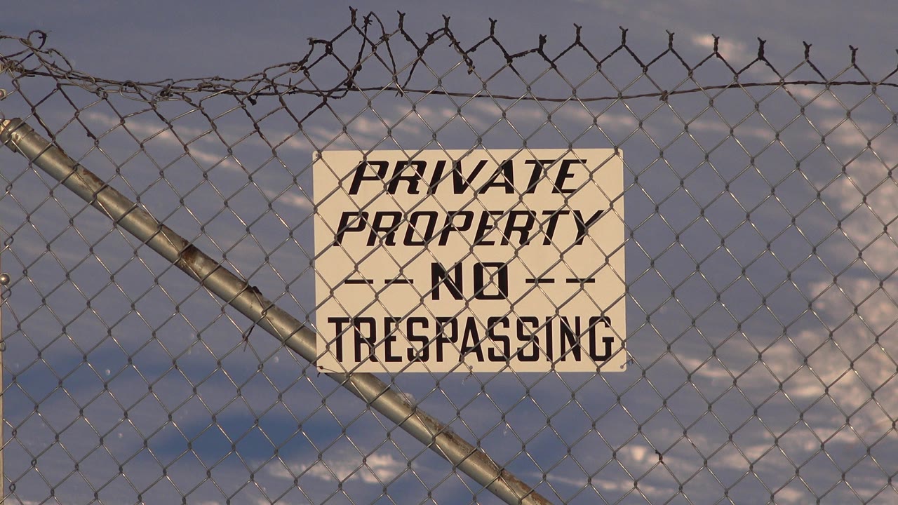 Second frame holds on the Private Property No Trespassing sign through the chain-link fence, with snow and soft evening light in the Westminster residential background and no visible people.