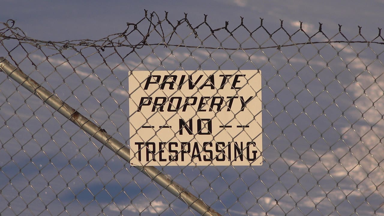 Opening frame of a white private property no trespassing sign attached to a chain-link fence in Westminster, Colorado, with barbed wire above and no visible people.