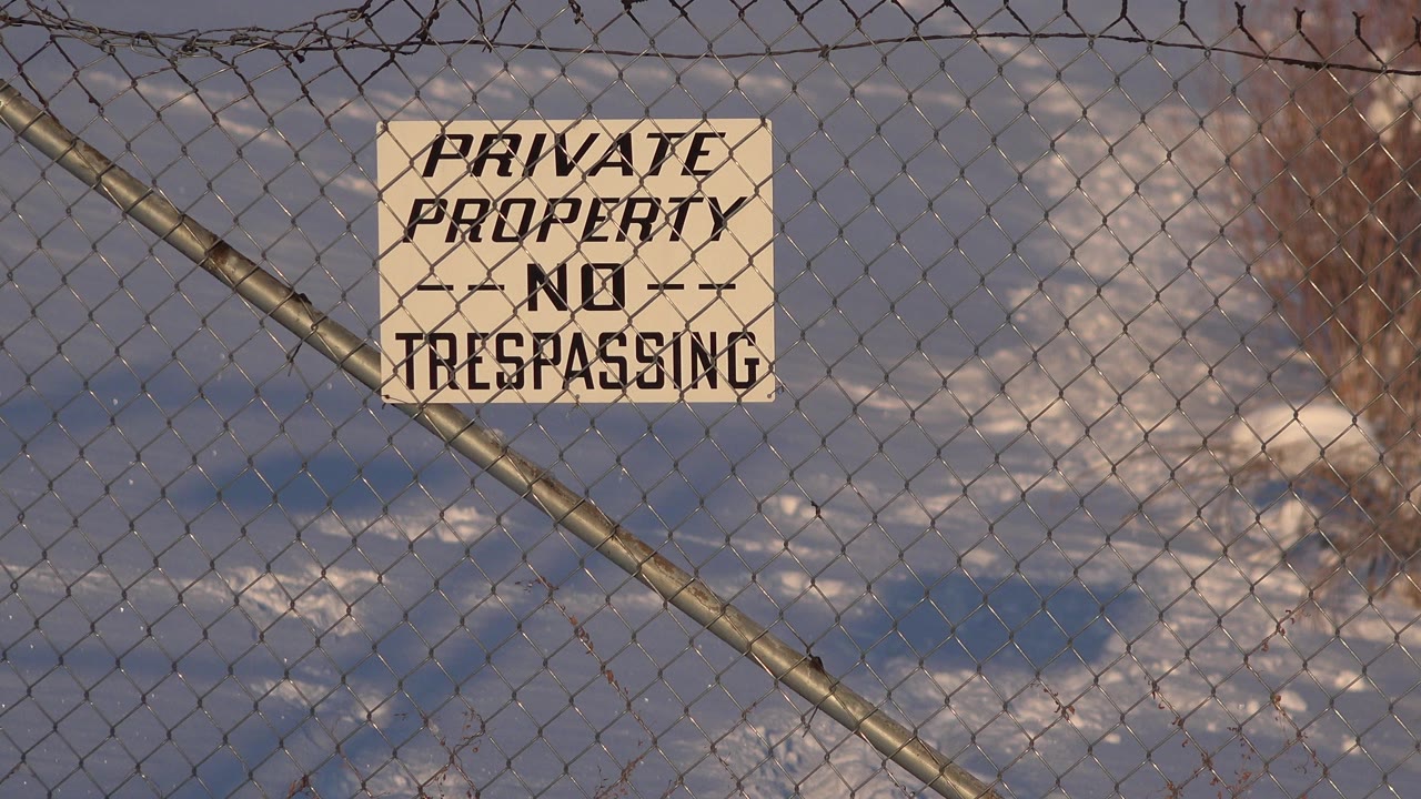Close frame of a Private Property No Trespassing sign fixed to a chain-link fence in Westminster, Colorado, with snowy ground and bare shrubs behind it and no visible people.