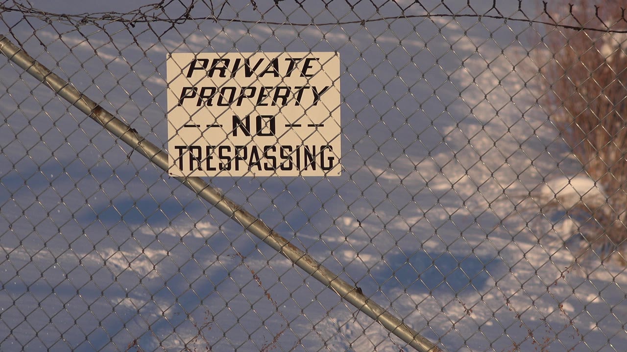 Slightly wider view of the Private Property No Trespassing sign on the fence in Westminster, Colorado, with blue shadows on snow and leafless brush in the background and no visible people.