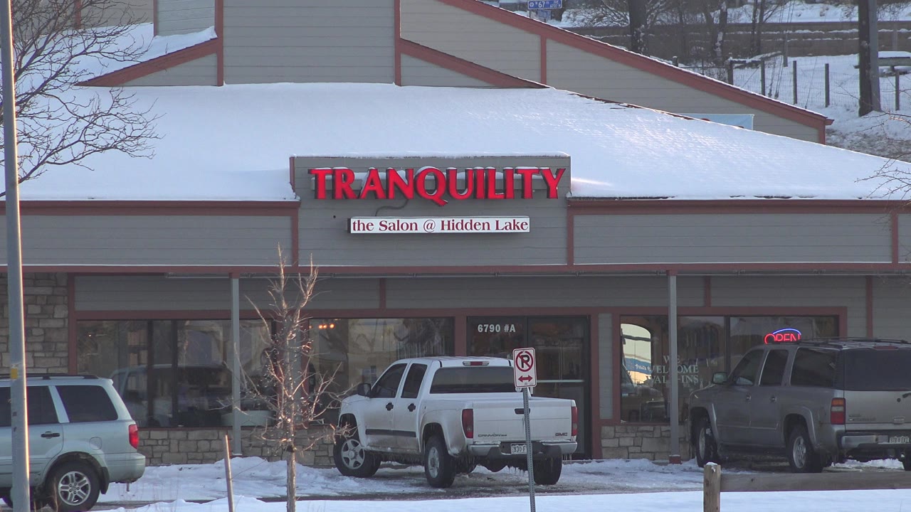 Snowy storefront with TRANQUILITY salon sign and parked trucks.