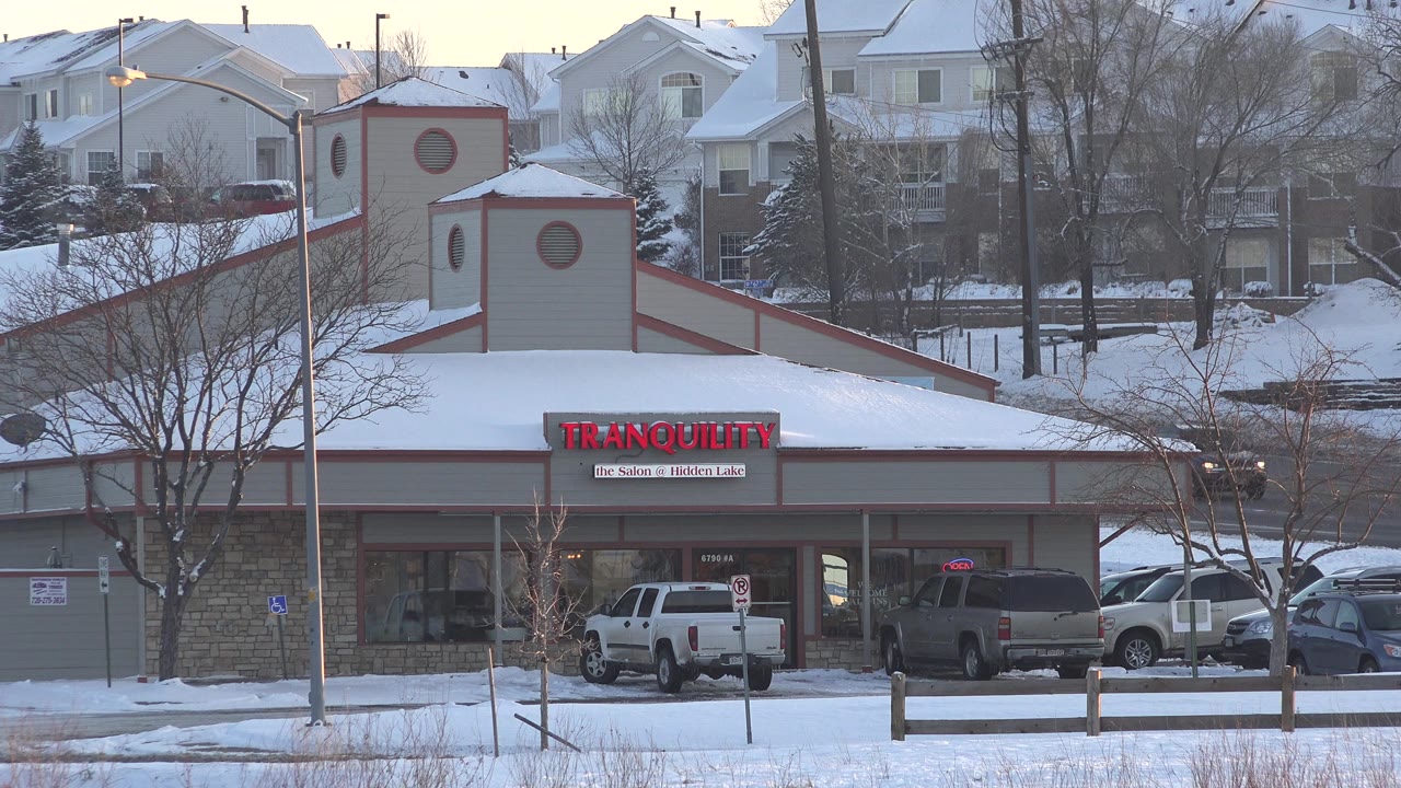 Westminster, Colorado retail building remains near center frame, with red Tranquility signage, snow-covered rooflines, parked cars, bare trees, and no visible people.