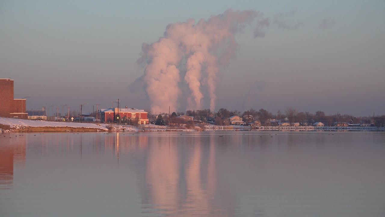 Industrial waterfront with broad white smoke cloud in the background.