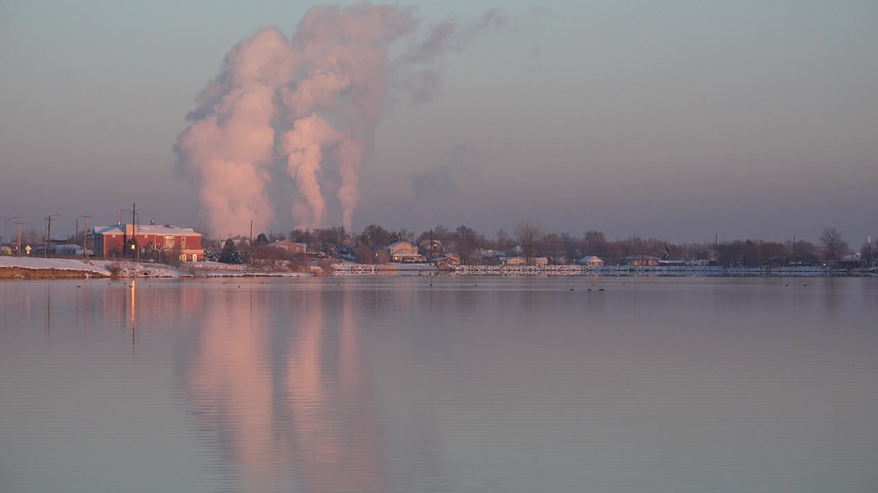 In Westminster, Colorado, the smoke column stands tall over the distant shoreline while the lake foreground stays smooth and reflective, with no visible people.