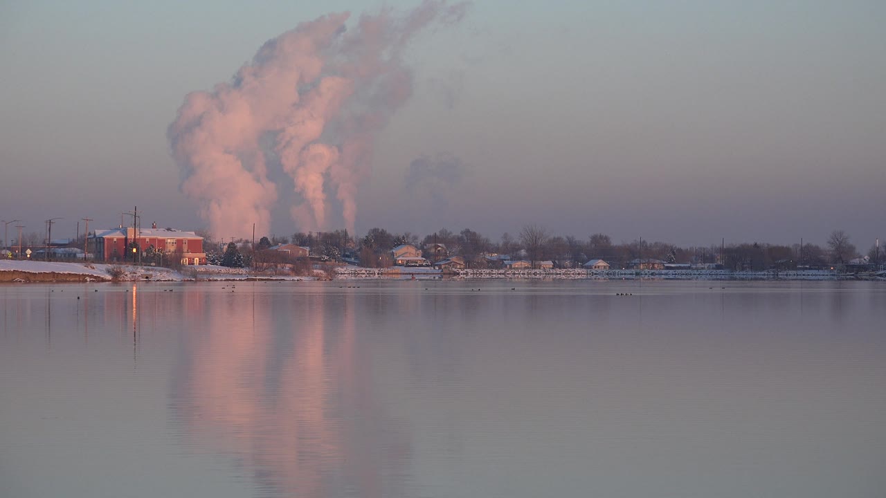 Distant snowy waterfront with red building and rising steam