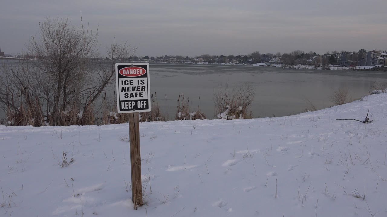 Thin ice warning sign beside a snowy frozen pond.