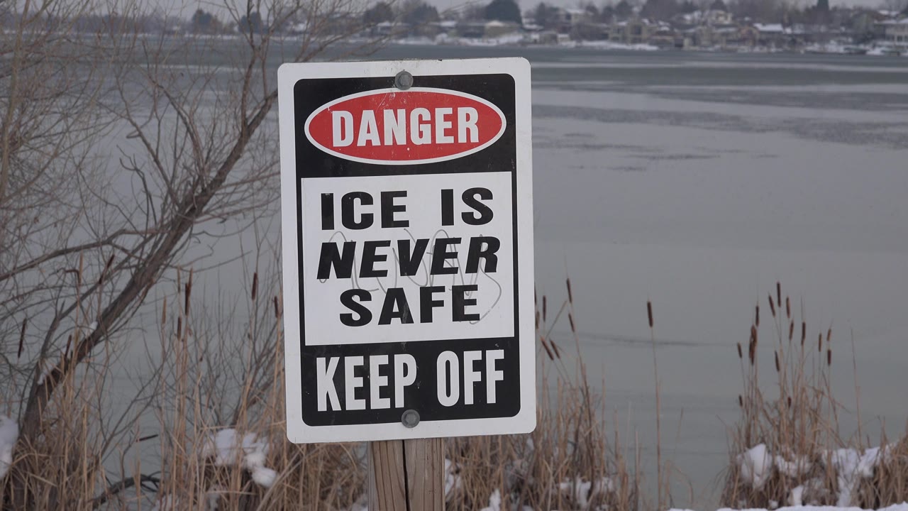 Danger ice warning sign beside frozen water and snow.