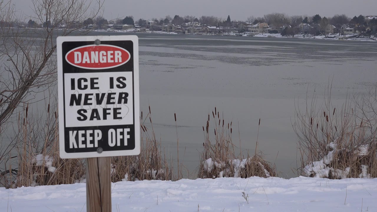 Ice danger warning sign beside a snowy lake shore.