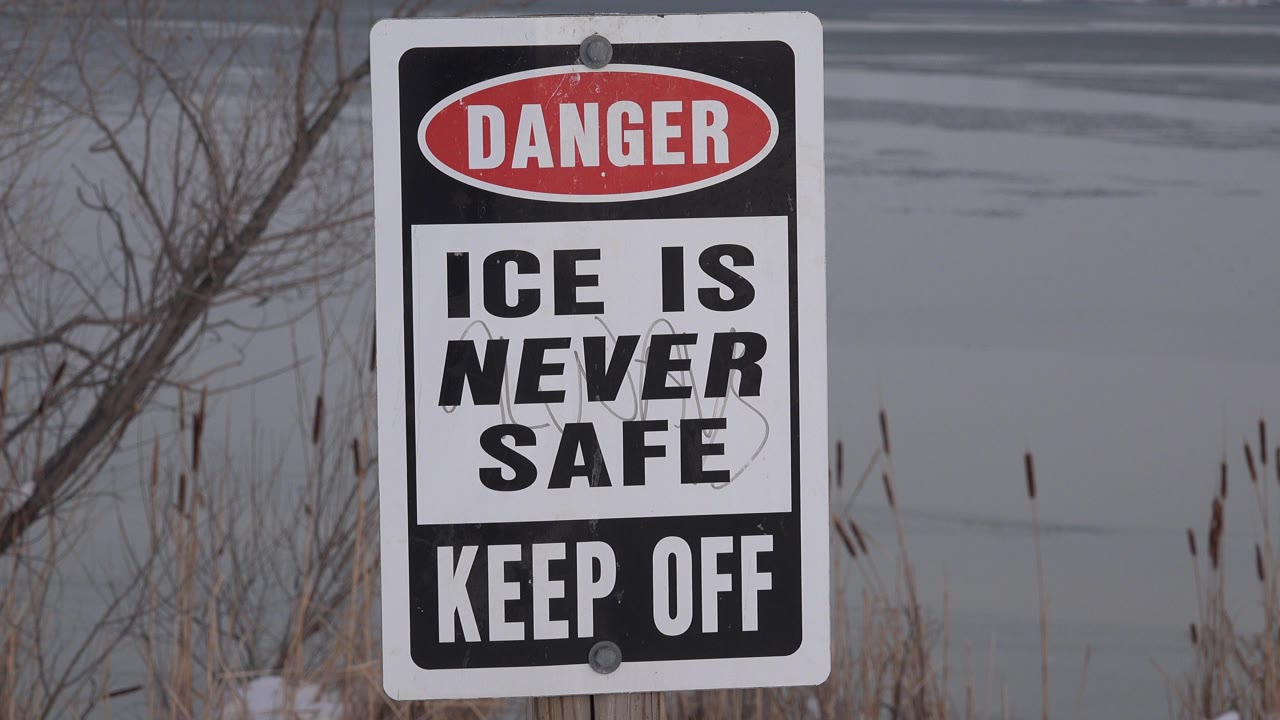 Danger ice warning sign beside frozen water.