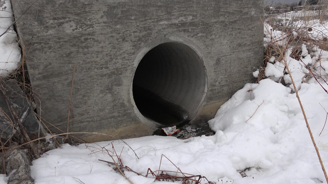 A large round concrete pipe opening sits in a gray wall with snow piled around it in Westminster, Colorado, with no visible people.