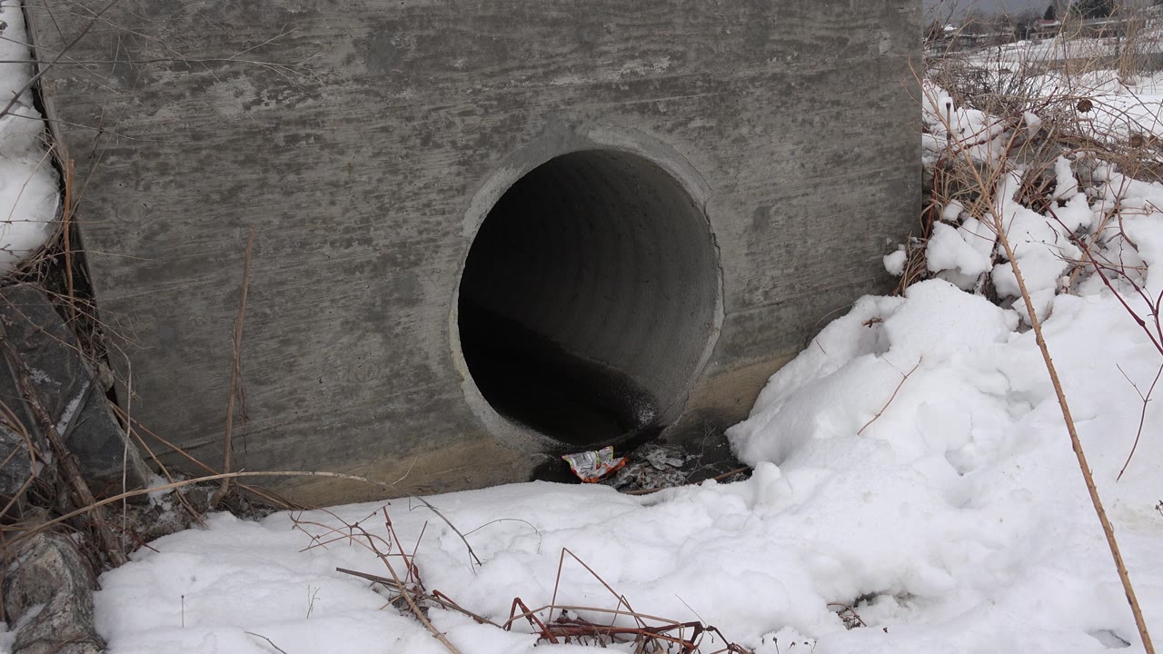 Round culvert-like pipe in concrete with snow piled to one side.