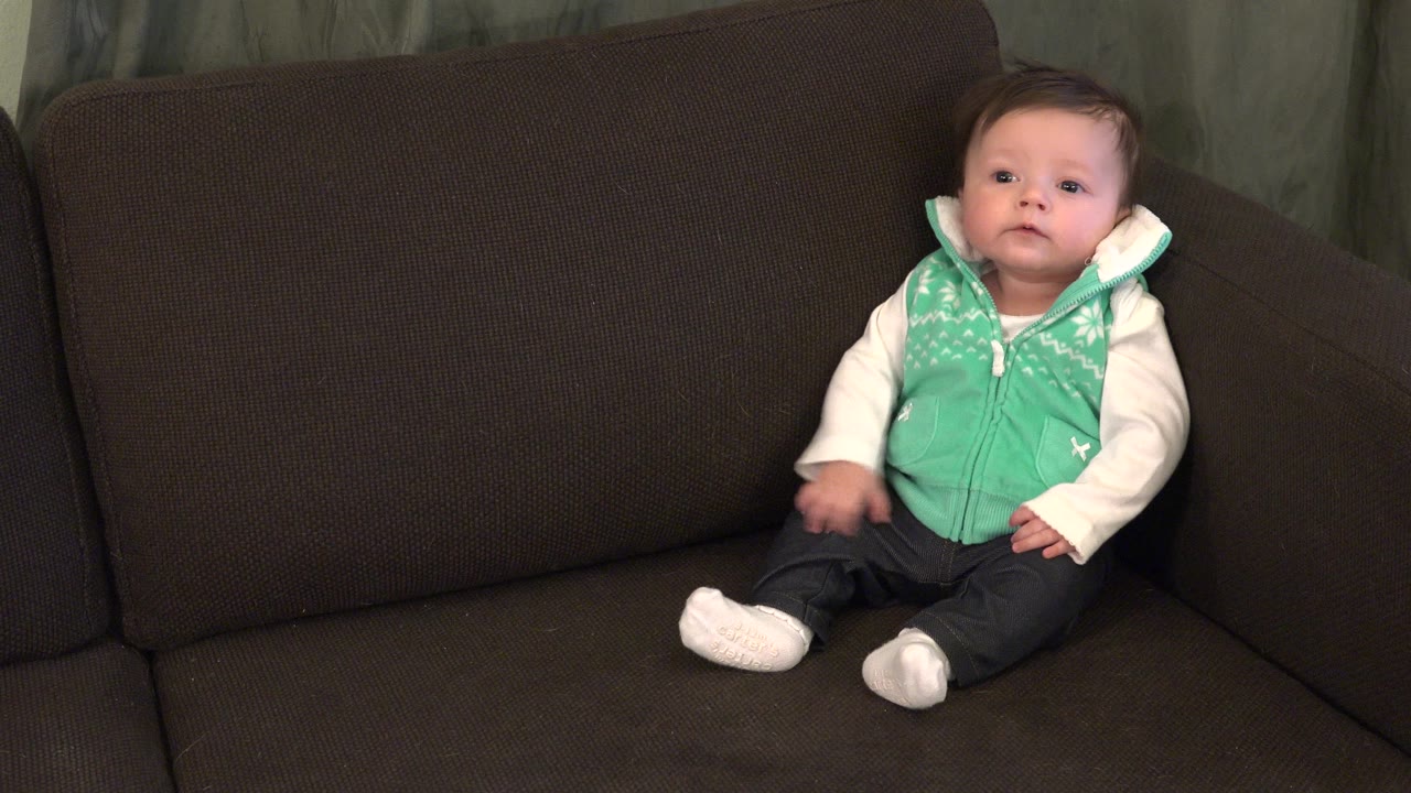 Baby in a green vest sitting on a brown sofa.