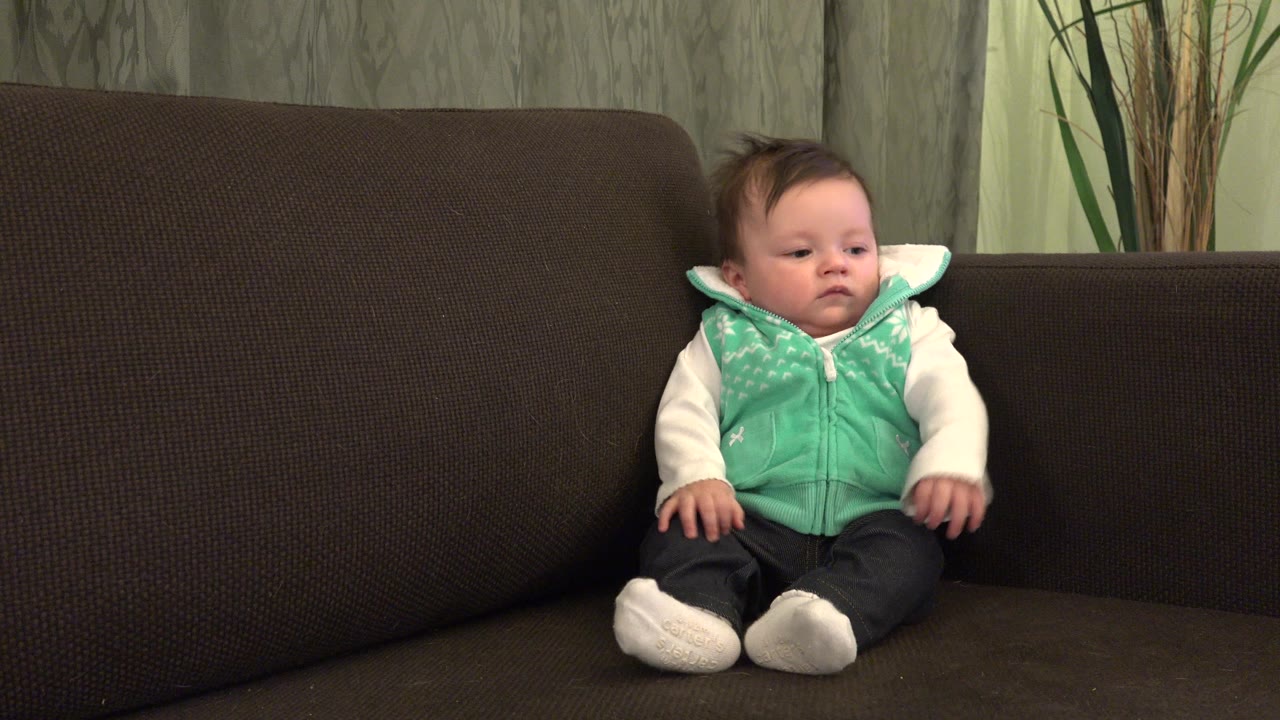 Baby sitting on a dark couch in a mint green vest.