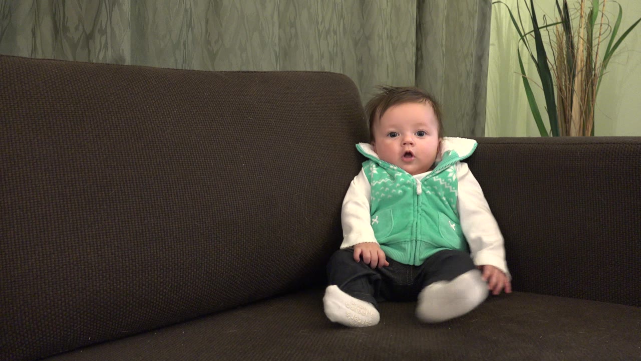 Baby sitting on a brown couch in a home interior.