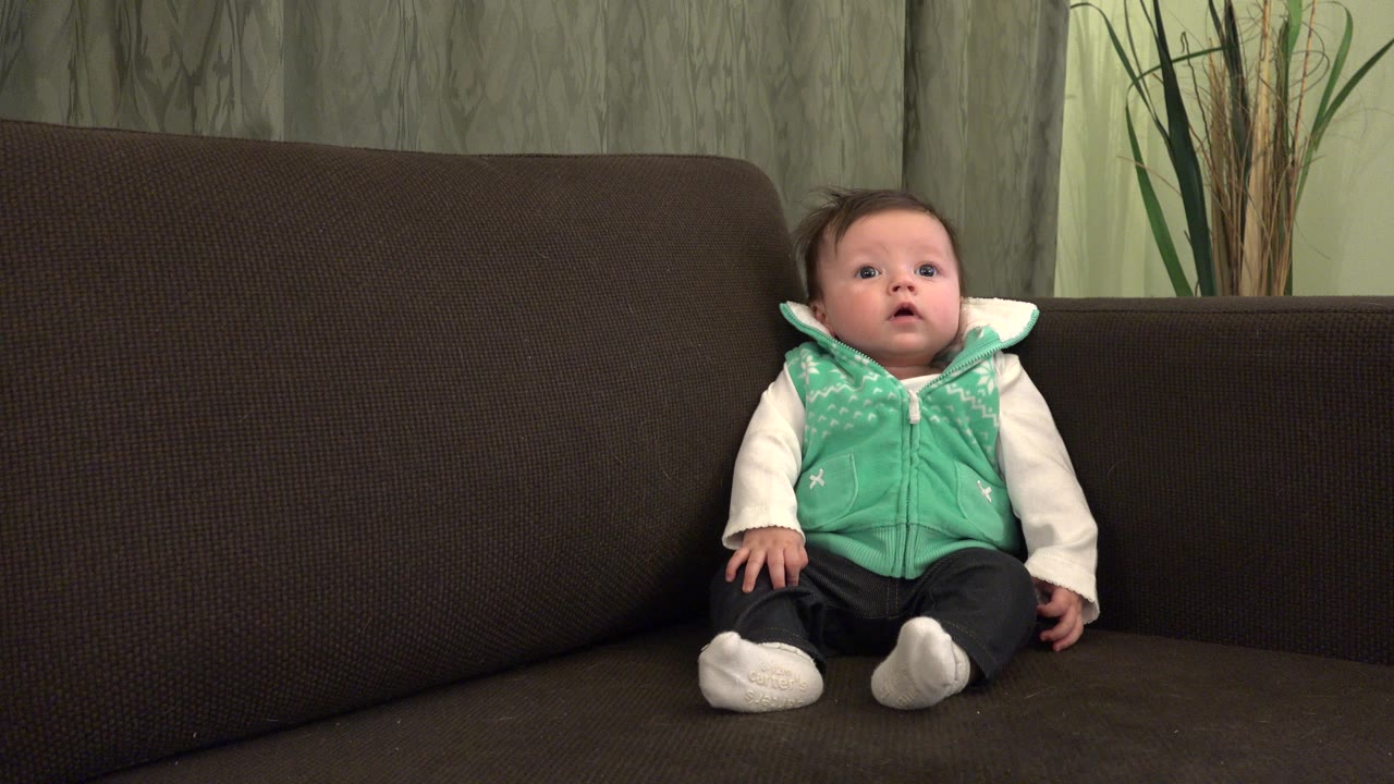Baby sitting on a dark couch in a living room.