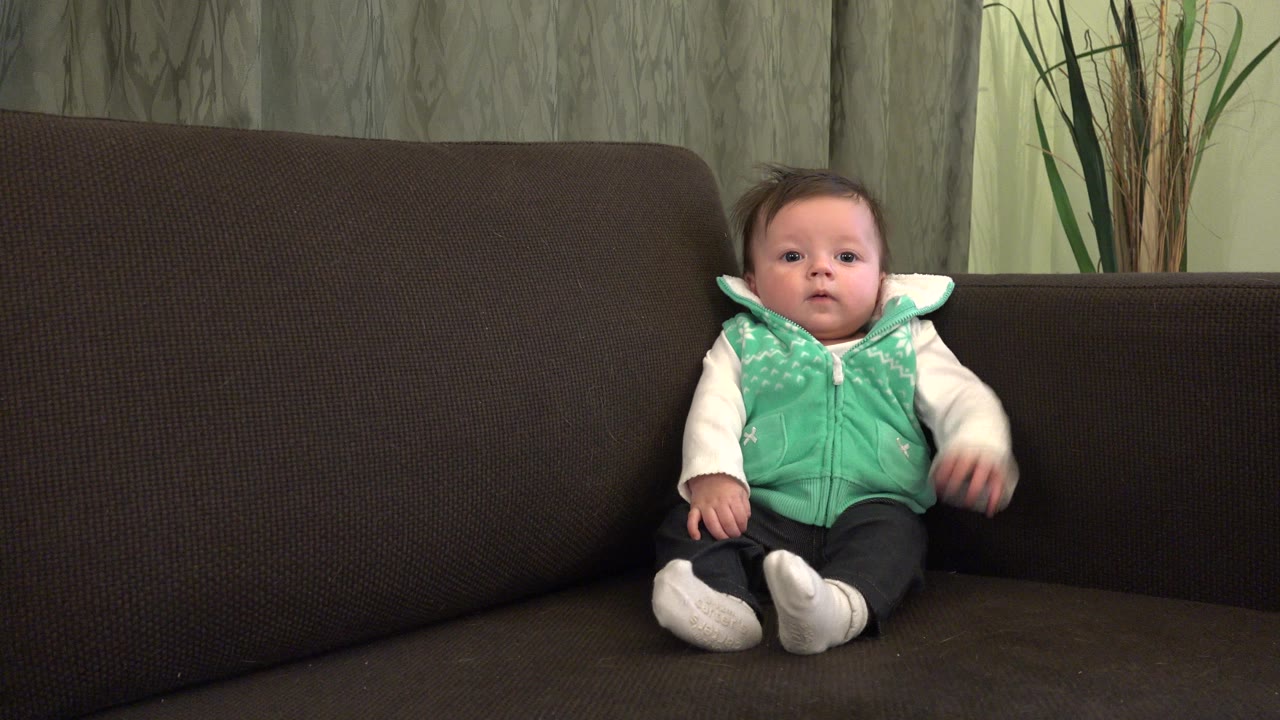 Young child seated on a dark sofa in a living room.