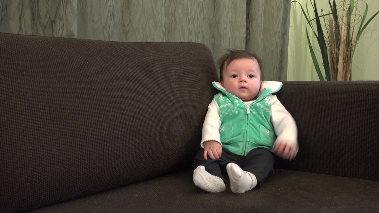 At 0:01, the child remains seated on the sofa in the Westminster, Colorado home, with one arm slightly lifted and the couch filling most of the frame.