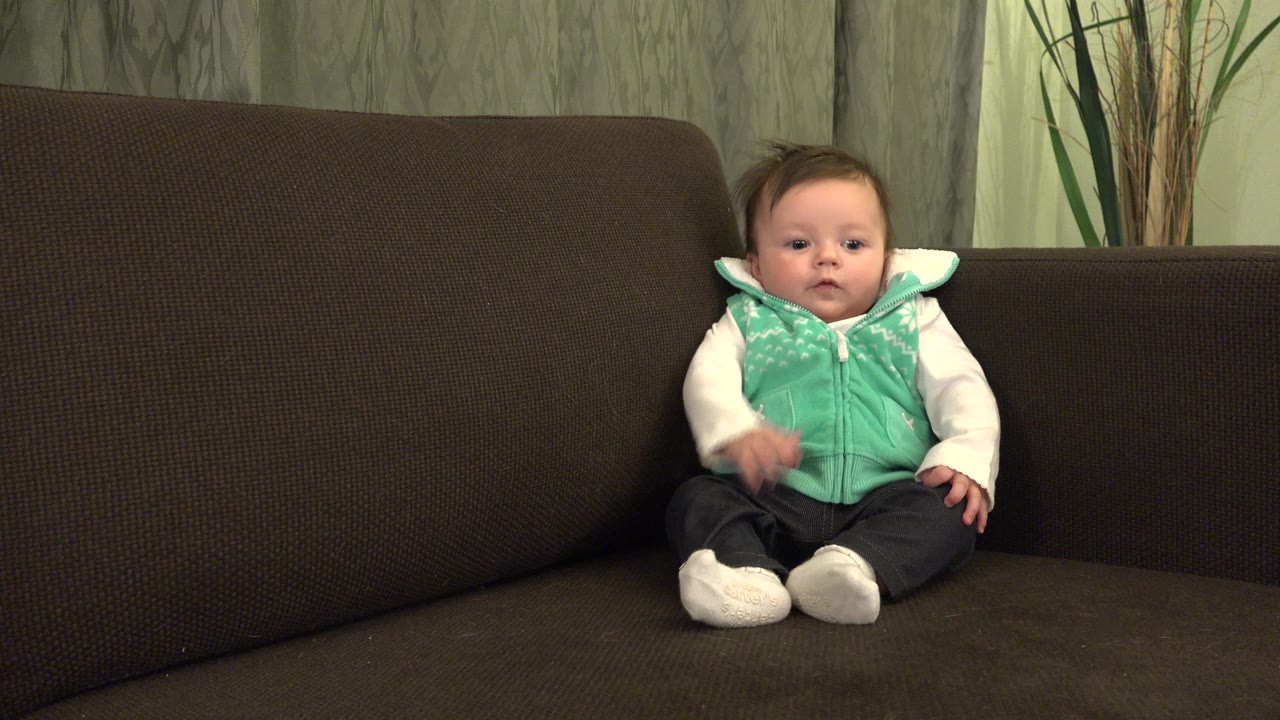 Baby sitting in the corner of a brown couch.