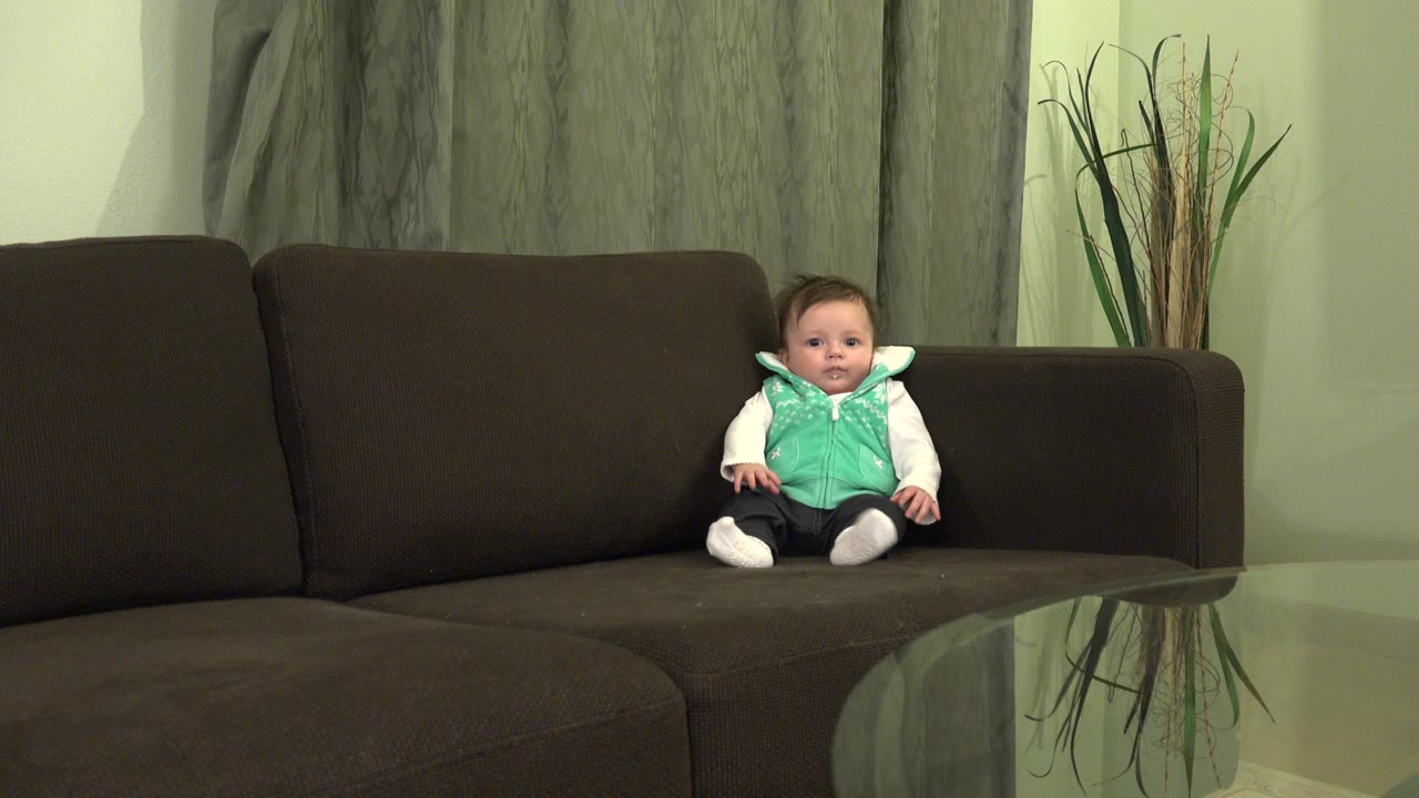 Baby sitting on a dark couch in a living room.