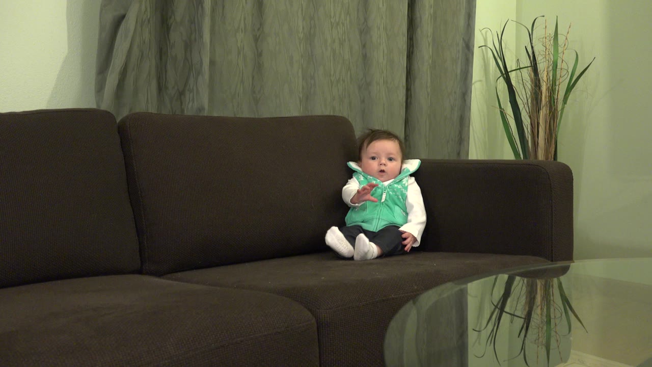 Baby boy sitting on a dark couch in a living room.