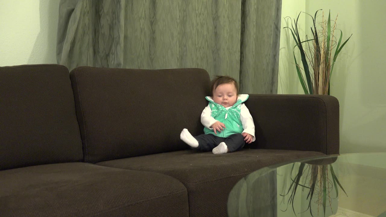 Baby seated on sofa with one leg raised.