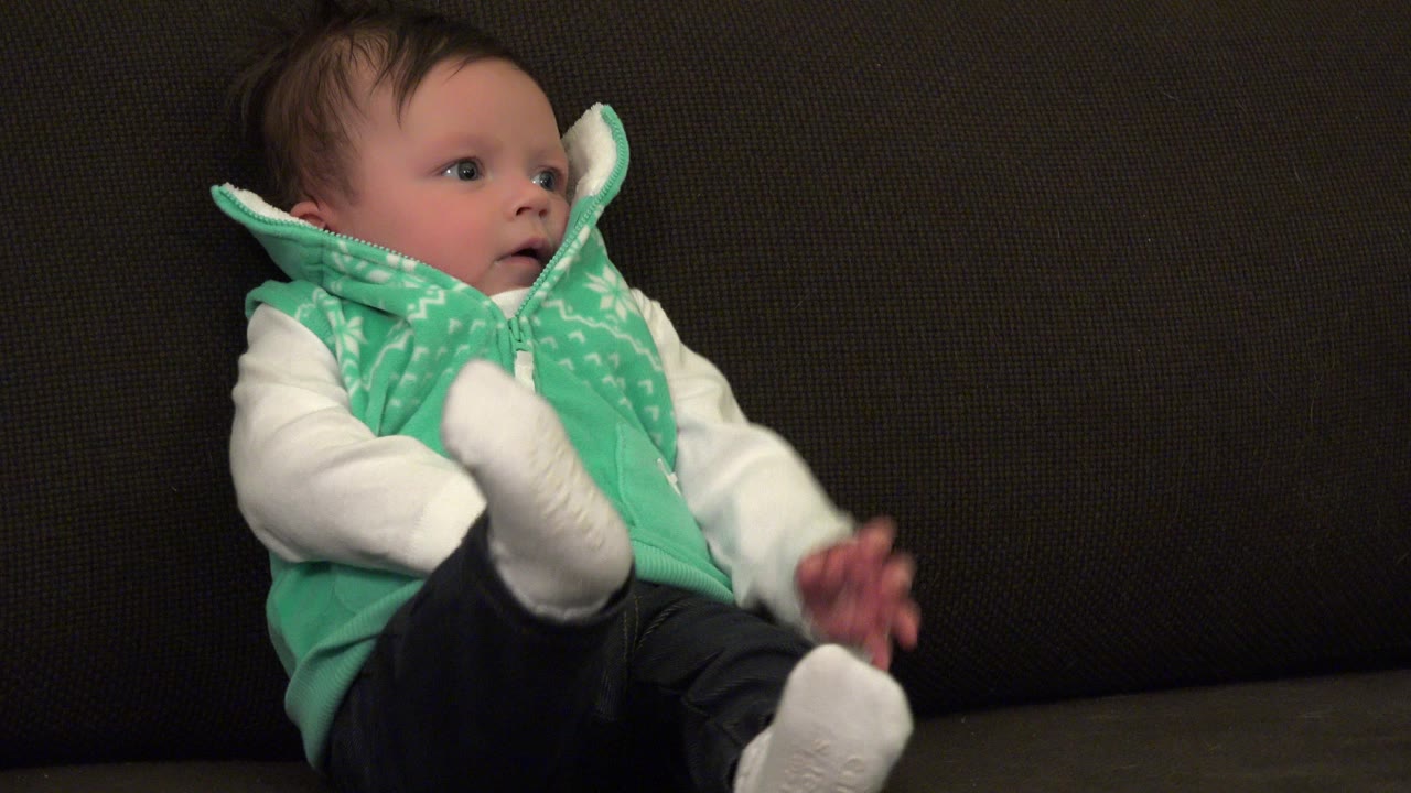 Infant in green vest sitting on a brown sofa.